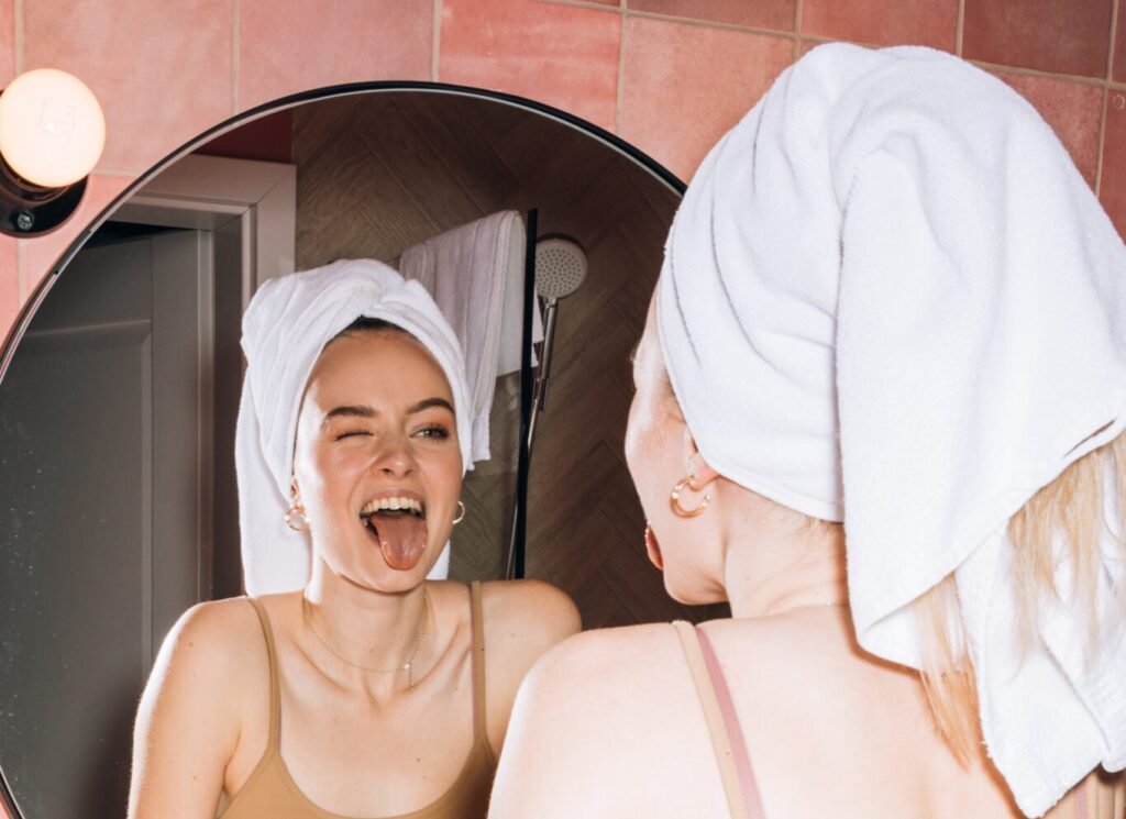 girl with towel in hair sticking tongue out in mirror