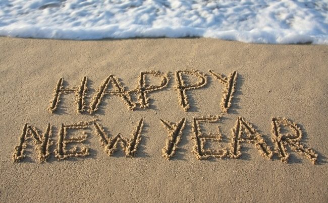 happy new year written in sand on th beach with waves