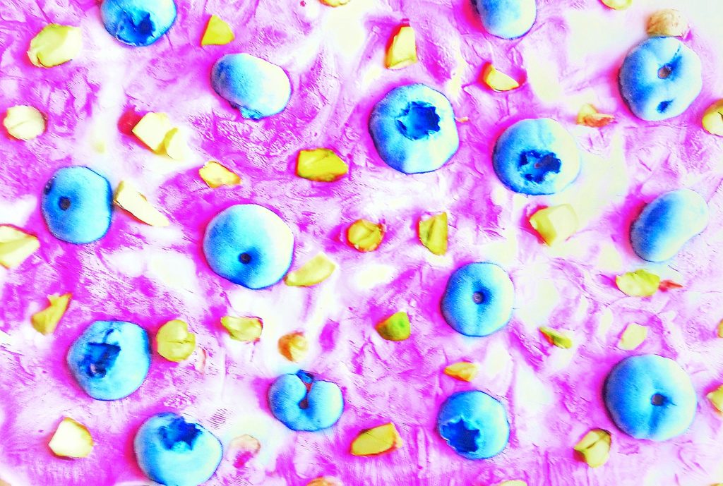 blueberries and pistachio scattered on top of frozen coconut hibiscus yogurt bark