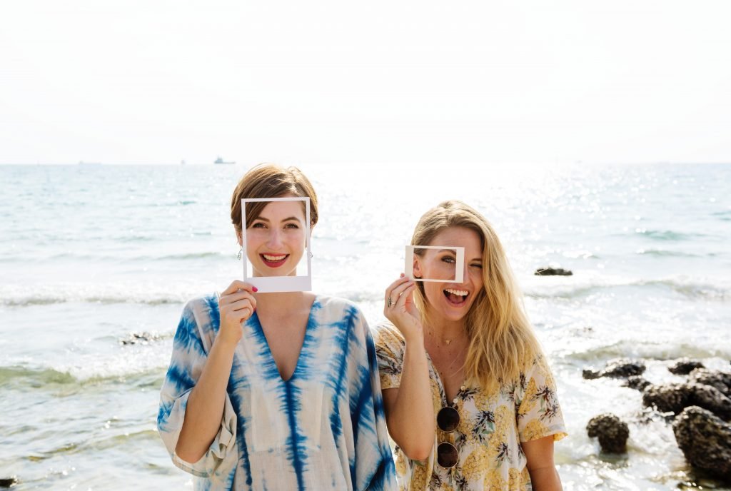 two women smiling with makeup and picture frames by the beach