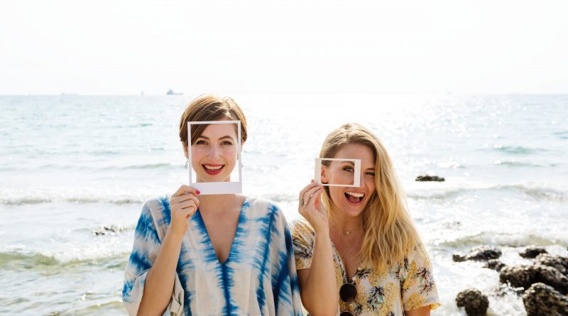 two women smiling with makeup and picture frames by the beach
