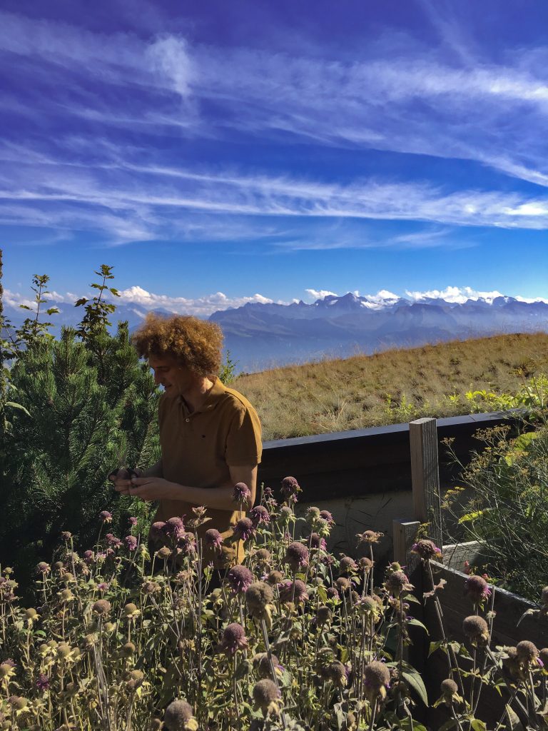 Krauter Hotel Edelweiss owner and herb specialist, Gregor Vörös, in the Alpine herb garden with secnis views the swiss alps behind