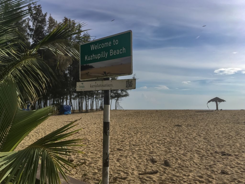 Signboard of Kuzhupilly Beach with palm trees and beach hut in the background