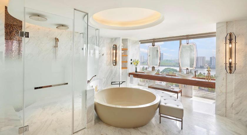 presidential suite bathroom at grand hyatt kochi with round bathtub with chaise lounge chair and separate shower cubicles in white marble