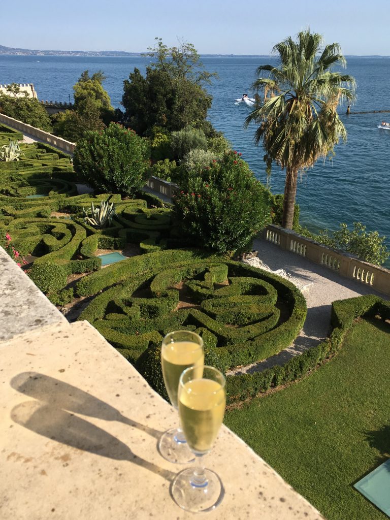two glasses of white wine atop the villa balcony of Isola della Garda overlooking the manicured gardens and lake garda