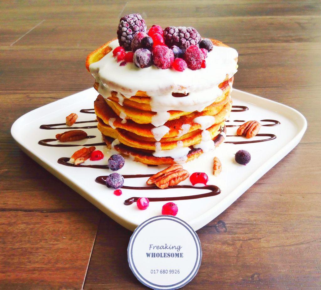 stack of banana pancakes topped with mixed berries and cream on a plate