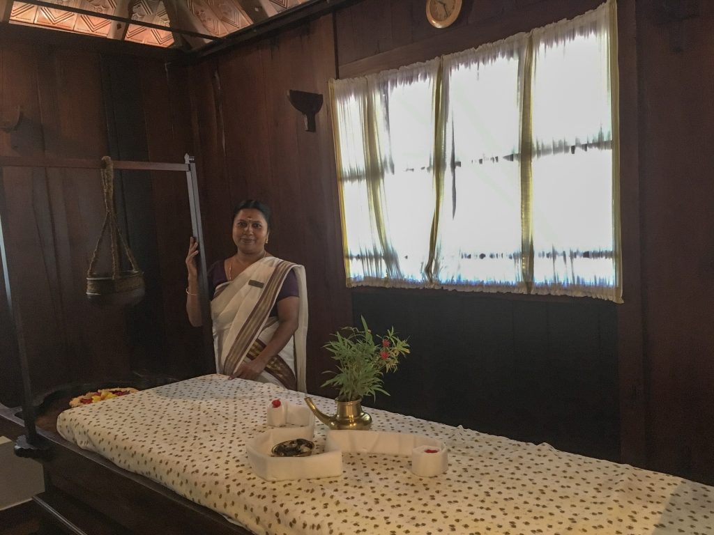 massage therapist in the wooden ayurveda spa room next to the shirodara pot and spa bed