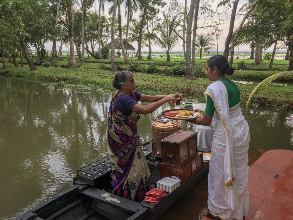 old indian lady in traditional sari serving tea from a small wodden boat to a waitress in sari