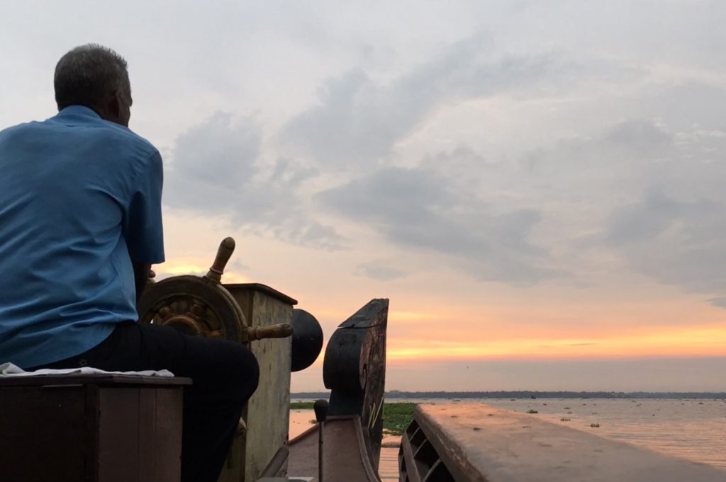 sunset cruise with boat driver behind the wheel watching the sunset on Lake Vembanad