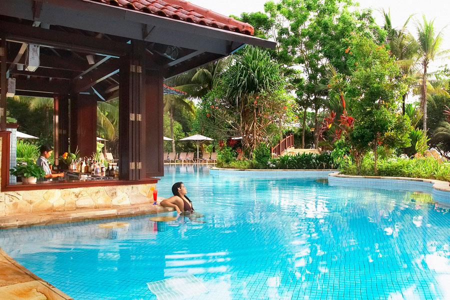 Bintan Lagoon Resort Poolside bar with bartender making cocktails and bikini girl relaxing in the swimming pool