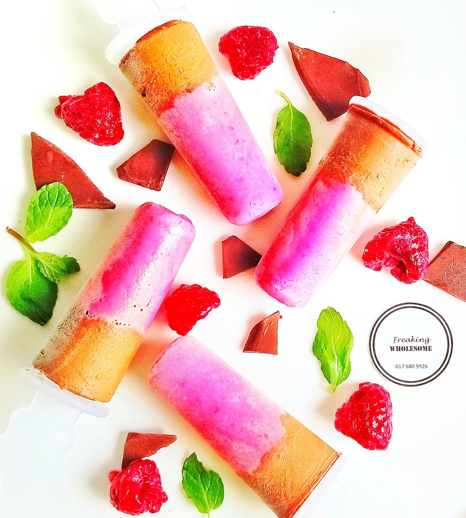 two layer minty chocolate raspberry popsicle ice cream cones with scattered mint leaves and raspberries 