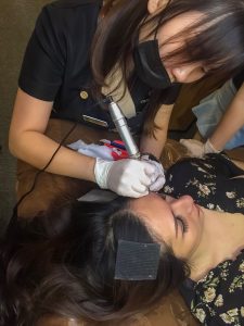 eyebrow embroidery technician performing mist semi permanent makeup using embroidery pen on woman