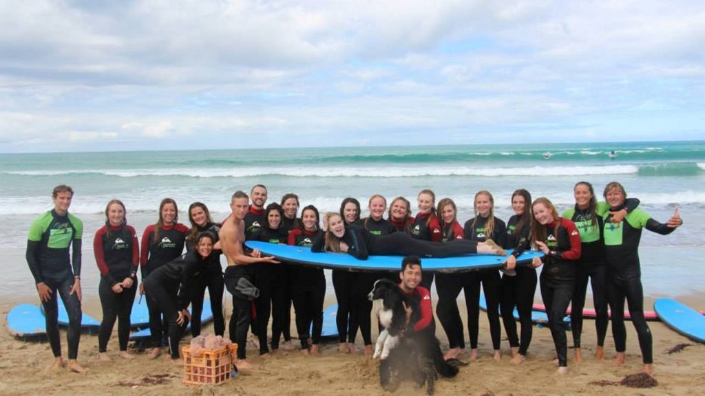 group of ladies and surf instructors having fun posing with a surfboard in Lorne for the best girly getaways in Victoria