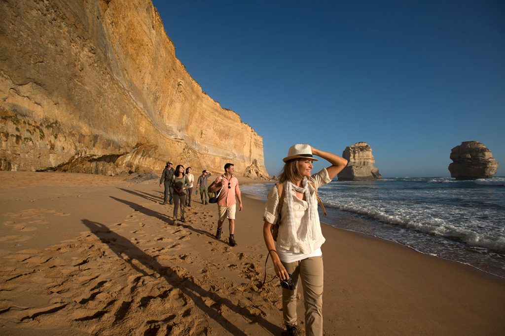 group of people trekking on the beach next to the 12 apostles in victoria