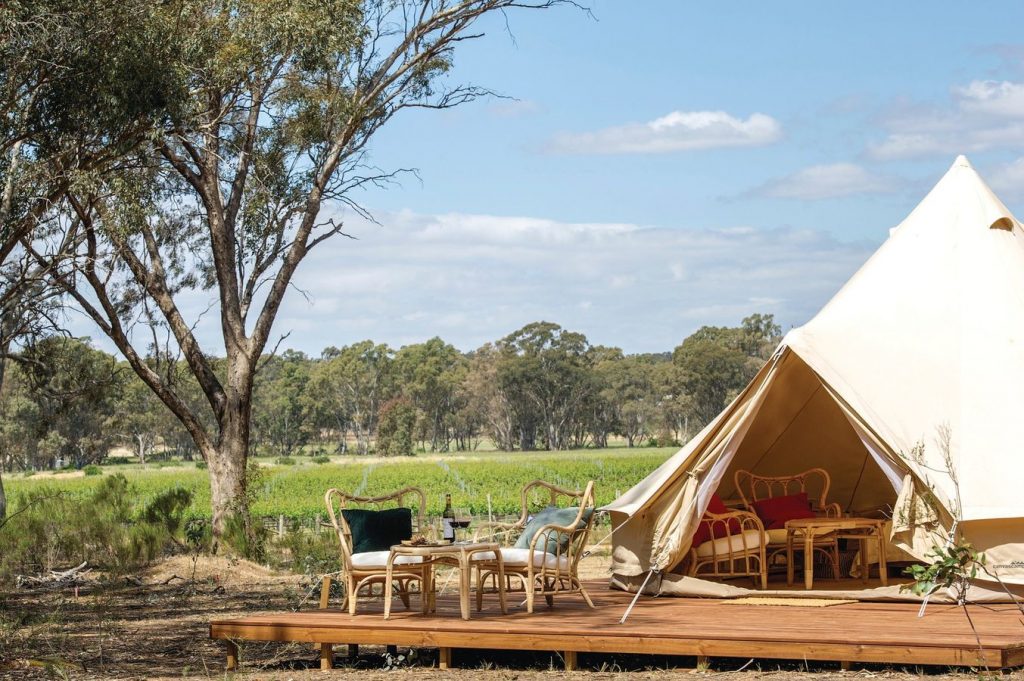 large white camping tent for glamping with outdoor patio and wine on table within a vineyard