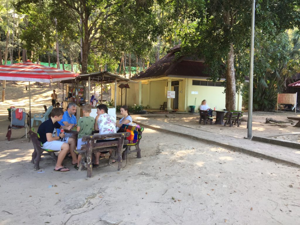 people sitting on the picnic table eating from the food and drinks stand at pasir tengkorak beach