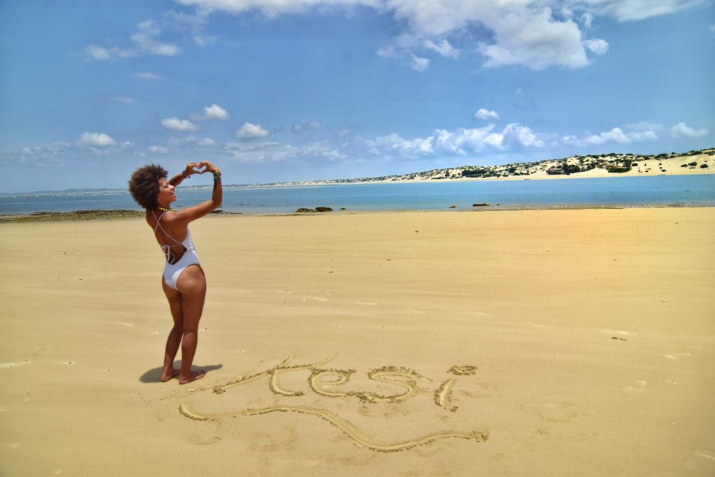woman with white swimwuit and heart hand sign on shela beach in lamu island