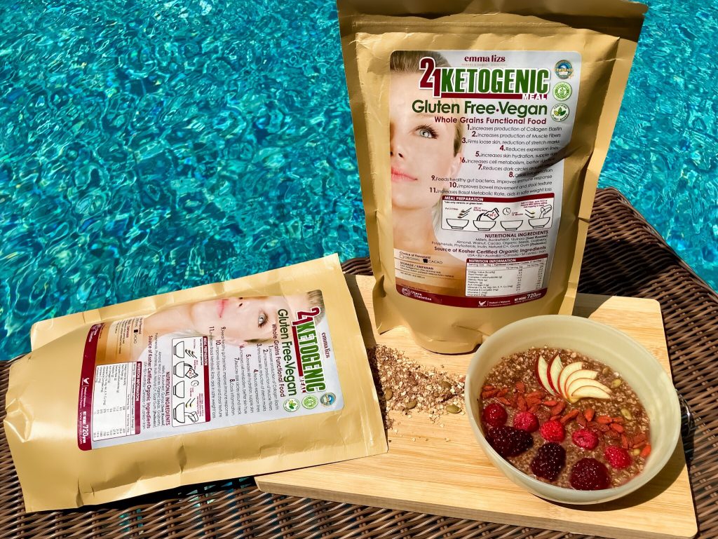 emma lizs 21 days ketogenic meal supplement packs on a wooden board with breakfast bowl of raw ingredients and fruits by the swimming pool