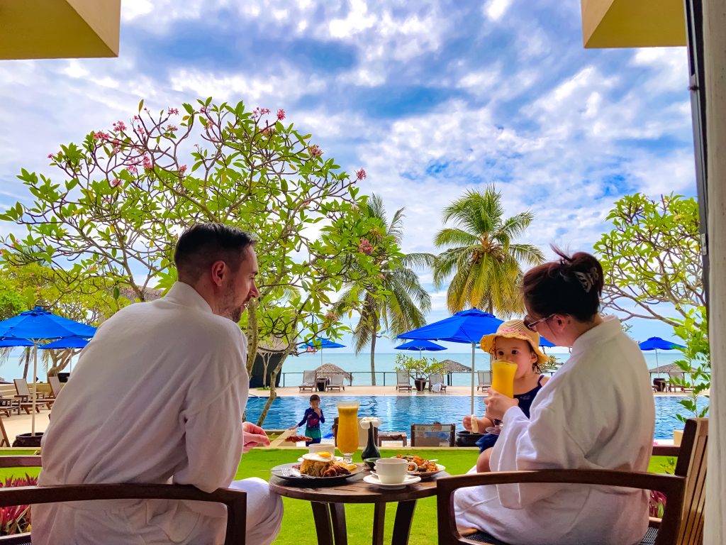 father mother in bathrobes and baby having malaysian breakfast by the poolside at hyatt kuantan