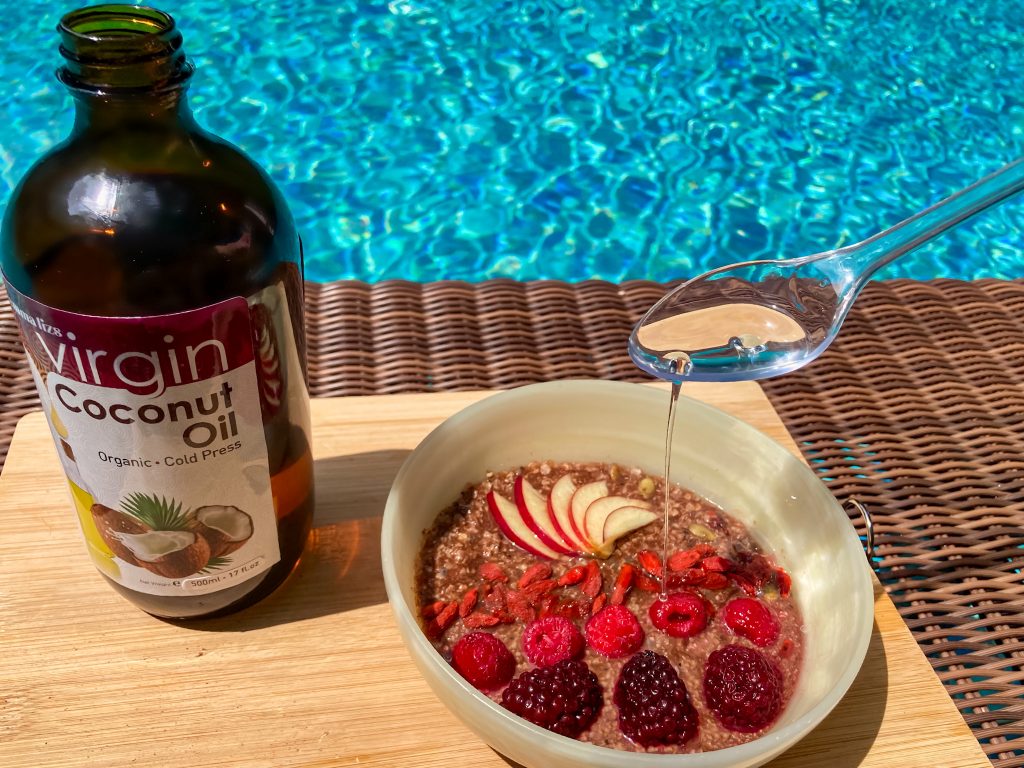 21 ketogenic meal breakfast bowl with fruits and a spoonful and a bottle of extra virgin coconut oil by the swimming pool